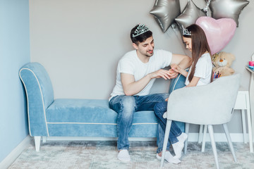 Handsome young father sitting on sofa  with his little cute girl. Daughter is doing nails  for her...