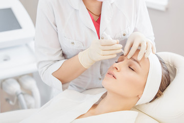 Obraz na płótnie Canvas Unidentified master cosmetologist makes botox injections into the eyebrow of a beautiful young woman client. The concept of rejuvenating aesthetic procedures
