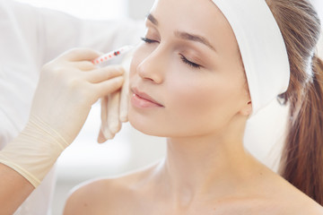 Female cosmetologist makes beauty shots to her client woman sitting on a couch. Concept of rejuvenating aesthetic salon procedures