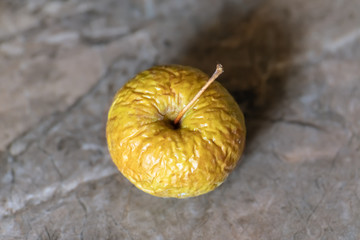 Wrinkled yellow old apple lies on the table top.