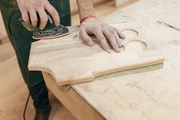 Hands of a professional woodman make a souvenir kitchen board with a tool with a cutter. Concept of profession carpenter builder