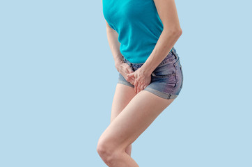 Young woman in shorts and a T-shirt is experiencing pain in the womb, pressed her hands to the lower abdomen. Medical concept. Gynecological problems