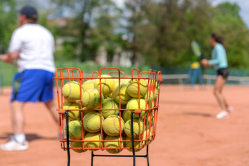 training camp for tennis players in tennis academy for men, women and young junior athletes, basket with yellow tennis balls foreground