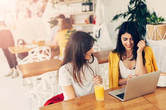 Attractive young georgian models sit in cafe. Spend time together. Remote work in coworking space. Attractive brunettes loook at each other and laptop.