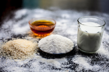 Face mask for flawless skin on wooden surface consisting of rice flour,corn flour,honey,milk, in a glass bowl and entire raw ingredients present on the surface.