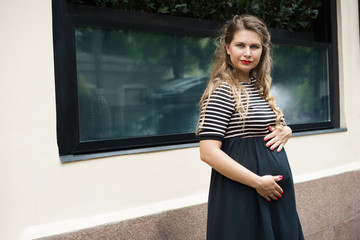 A pregnant woman in a black and white striped dress with long blond hair folded her hands on her...