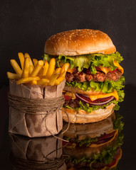 A large rustic Hamburger and French fries on a dark wooden table. Fast food.