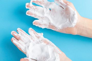 Teenager washes his hands with foam soap on a blue bright background