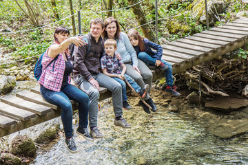 happy family are sitting on a wooden bridge in a forest  and are doing a selfie