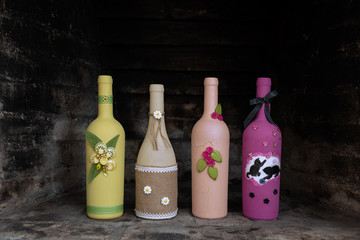 A line of four hand-painted empty wine bottles with individual decorative designs set in a blackened stone fireplace