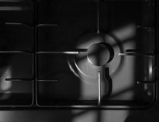 Overhead monochrome semi-abstract close-up of a section of gas-hob showing the ring and lines in directional natural daylight with varying shades of grey.