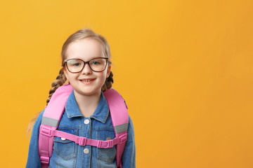 Portrait of a little girl schoolgirl with a backpack on a yellow background. Child with glasses close-up. Back to school. The concept of education.