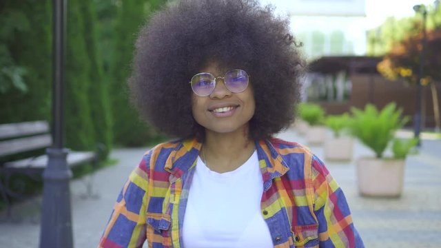 african woman with an afro hairstyle disabled in a wheelchair looking at the camera and smiling against the urban landscape