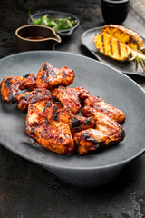 Exotically barbecue chicken wings with hot chili sauce, jalapeno and pineapple as closeup on a cast iron plate