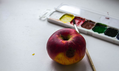 a red apple and watercolor paint and brush on white background