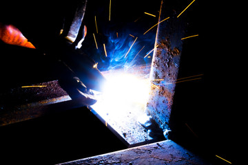 Welder worker performs jump welding. Man welder in protective gloves performs arc-welding process of metal structures. Flying sparks from the welding machine. Background construction site