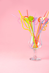 Multicolored plastic cocktail straws in an empty glass cup on a pink background. Concept: holiday, party, ecology, plastic