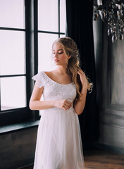 Fototapeta premium gentle image of graduate, sweet girl with natural make-up in long white vintage dress with bare shoulders, lady with curled light hair in dark magic castle, court lady waiting for meeting with prince.