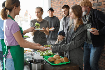 Volunteers giving food to poor people indoors