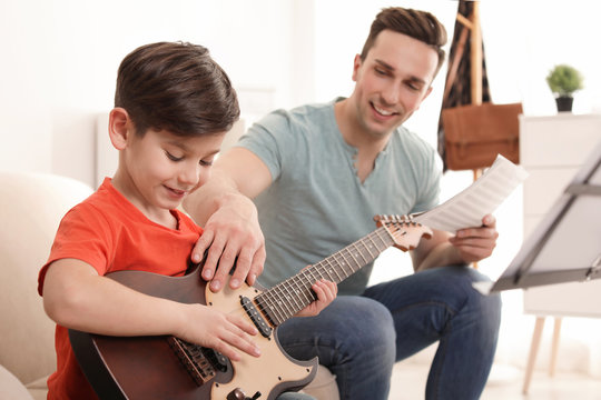 Little boy playing guitar with his teacher at music lesson. Learning notes