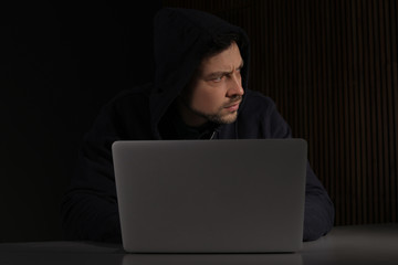 Man using laptop in dark room. Criminal offence
