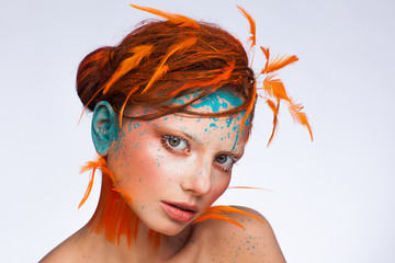 Portrait of a beautiful model with creative make-up and hairstyle using orange feathers