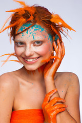 Portrait of a beautiful model with creative make-up and hairstyle using orange feathers