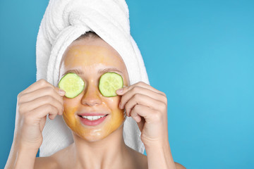 Beautiful woman holding cucumber slices near her face with natural mask against color background. Space for text
