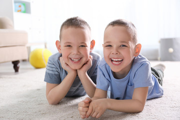 Portrait of cute twin brothers on floor in living room - obrazy, fototapety, plakaty