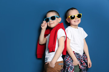Portrait of cute twin brothers with sunglasses on color background. Space for text