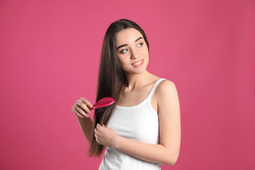 Beautiful smiling young woman with hair brush on color background