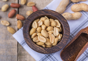 Peanuts in small dark wooden bowl on natural rustic desk.