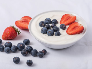 White yogurt in bowl with strawberries, blueberries on the top on white background.