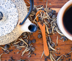 A close up of teapot, cup and red tea, green tea and white tea leaves on a wooden table