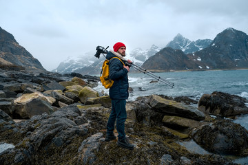 Young man photographer standing at rock in the mountains at Beach photographing the landscapes on Lofoten Islands in Norway.