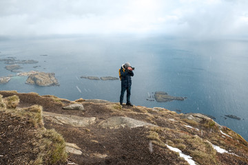 Young man photographer standing at rock in the mountains at Beach photographing the landscapes on Lofoten Islands in Norway.