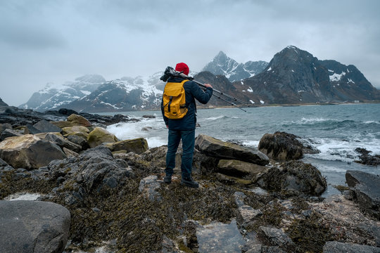 Young man photographer standing at rock in the mountains at Beach photographing the landscapes on Lofoten Islands in Norway.