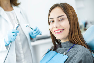 A woman is smiling with white and healthy teeth while sitting in a dental chair. Doctor dentist and happy patient in the office of a medical clinic.