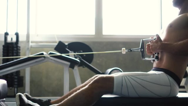 Shirtless muscular young man doing seated cable row exercise on machine at the gym