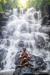 Fototapeta na wymiar Woman practices yoga near waterfall in Bali, Indonesia
