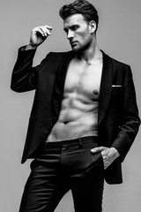 Portrait of a shirtless young and handsome model in a black suit. Studio shot. Copy space