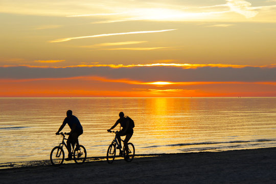 couple riding a bicycles and sunset over the sea on background