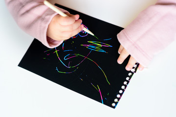 Close up of Happy girl hands drawing on magic scratch colorful painting paper with drawing stick.