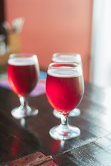 Three glasses with red wine on a wooden table. Glasses of cherry beer are on the table. There is no one in the frame.