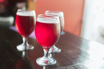 Three glasses with red wine on a wooden table. Glasses of cherry beer are on the table. There is no one in the frame.