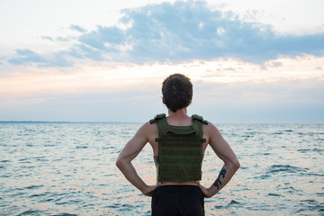 Young bearded athlete training outdoor with weighted vest,  exercise with military plate carrier