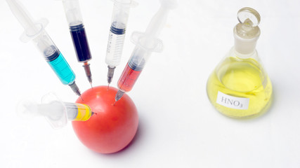 Tomato and syringe with nitrates. GMO food ingredient concept.