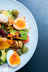 Healthy vegetables green caesar or greek mediterranean salad with boiled egg and fruits in white porcelain dish on table for vegetarian on black background from top view.