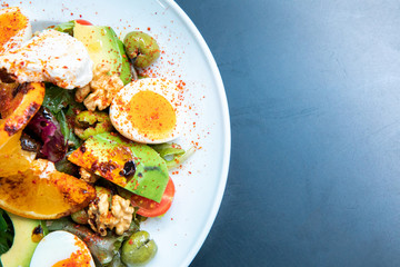 Healthy vegetables green caesar or greek mediterranean salad with boiled egg and fruits in white porcelain dish on table for vegetarian on black background from top view.