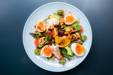 Healthy vegetables green caesar or greek mediterranean salad with boiled egg and fruits in white porcelain dish on table for vegetarian on black background from top view.